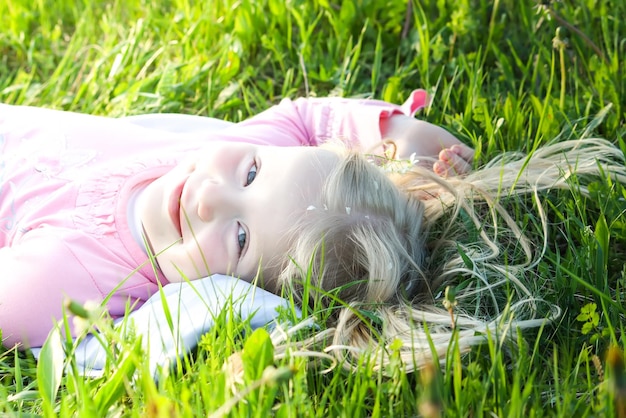 Schattig klein blond meisje met witte bloemblaadjes van gewone vogelkers op haar haar liggend op de groene weide in het voorjaarspark