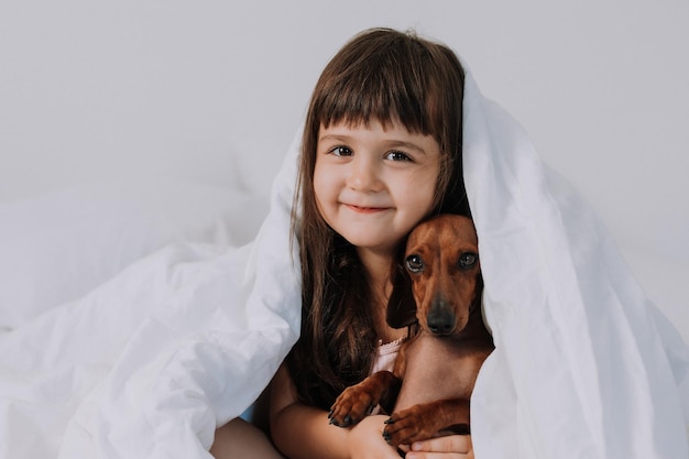 schattig klein brunette meisje thuis in bed met een bruine teckel hond knuffelen en slapen