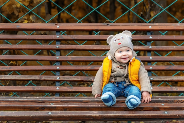 Schattig klein eenjarig kind op een bankje in het park. Portret van een lachende peuterjongen. Wandelen in het herfstpark.