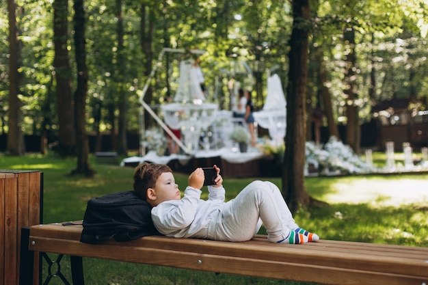 Foto schattig klein europees kind gericht op smartphone in een bankje in het park