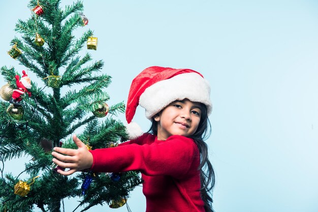Schattig klein Indiaas Aziatisch meisje dat Kerstmis viert en boom knuffelt over blauwe achtergrond