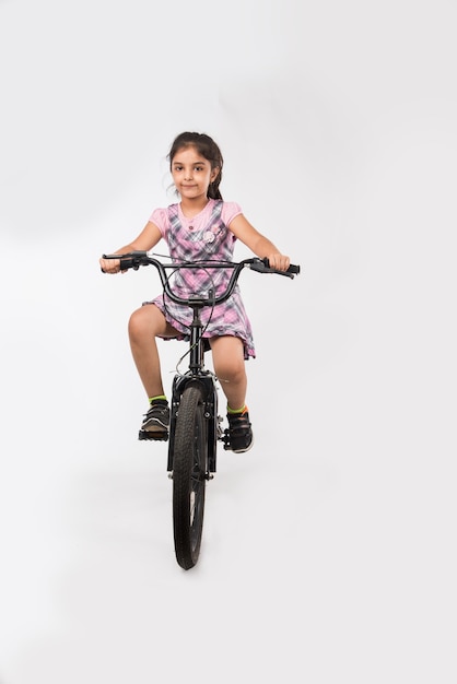 Schattig klein Indiaas of Aziatisch meisje dat op de fiets rijdt, geïsoleerd op een witte achtergrond met ballonnen