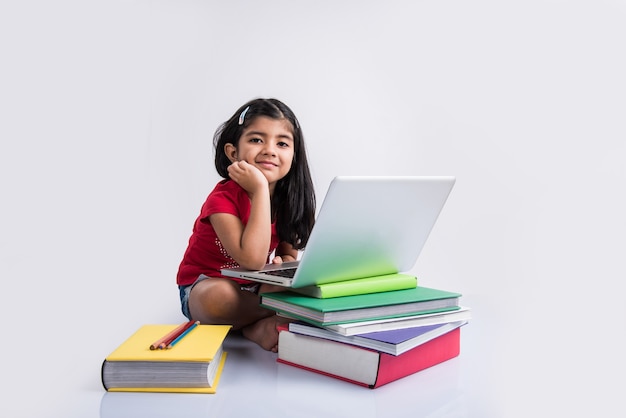 Schattig klein Indiaas of Aziatisch meisje dat op laptop studeert of aan een schoolproject werkt terwijl liggend of zittend op de vloer, geïsoleerd op witte achtergrond