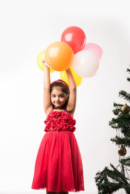 Schattig klein Indiaas of Aziatisch meisje met kleurrijke ballonnen of gubbare in het Hindi, op witte of rode achtergrond