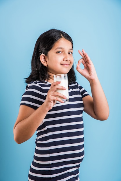 Schattig klein Indiaas of Aziatisch speels meisje dat een glas melk vasthoudt of drinkt, geïsoleerd op een kleurrijke achtergrond