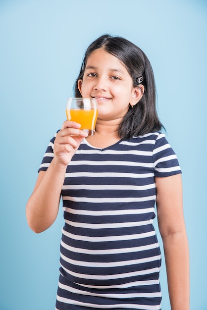 Schattig klein Indiaas of Aziatisch speels meisje dat verse mango of sinaasappelsap of koud drankje of drankje drinkt in een glas, geïsoleerd op witte achtergrond