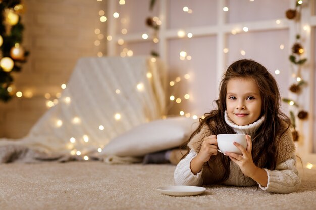 Schattig klein kind meisje drinkt warme chocolademelk uit grote beker thuis