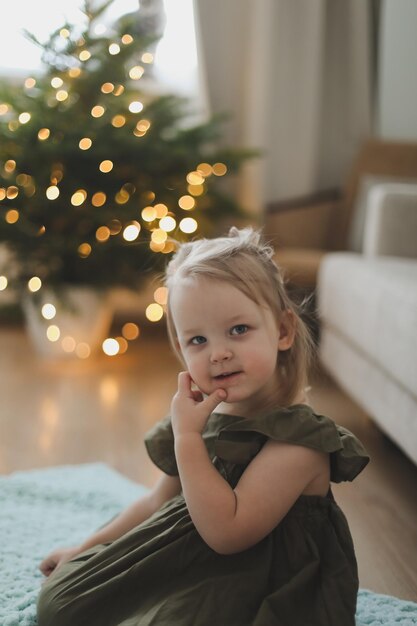 Schattig klein kind meisje en de kerstboom binnenshuis Prettige Kerstdagen en Gelukkig Nieuwjaar concept