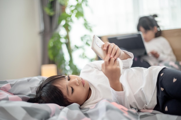 Schattig klein kind meisje kijken naar video op smartphone met smileygezicht alleen op het bed kind met behulp van mobiele telefoon met blij gezicht thuis Blijf thuis quarantaine coronavirus COVID19 pandemie preventie