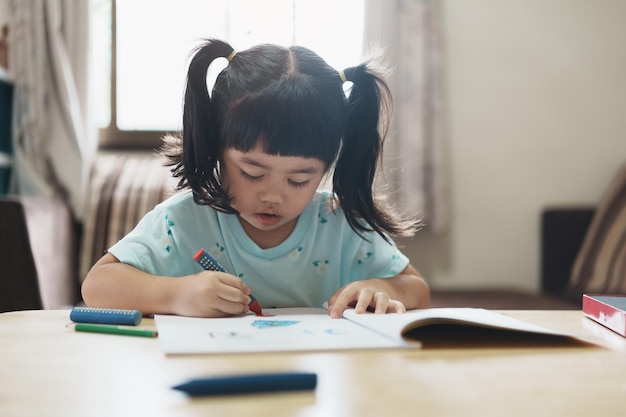 Schattig klein kind met een roze shirt met potlood of huiswerk of houtkleur schilderen met kleurrijke verf Aziatisch meisje met behulp van houtkleur tekening kleurBaby kunstenaar activiteit levensstijl concept