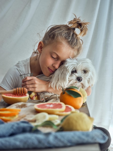 Schattig klein kind met gesloten ogen genietend van het gezelschap van witte pluizige kleine hond terwijl hij fruitlimonade maakt