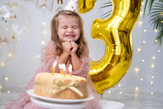 Schattig klein kindmeisje blaast kaarsen op verjaardagstaart en viert verjaardag