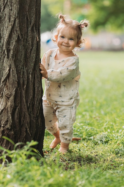 schattig klein lachend meisje met een grappig kapsel verstopt zich achter bomen en rent en speelt in het park