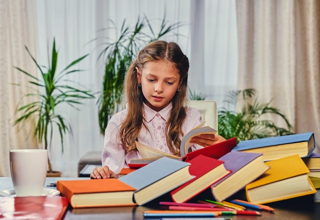 Schattig klein meisje aan de tafel met veel kleurrijke boeken.