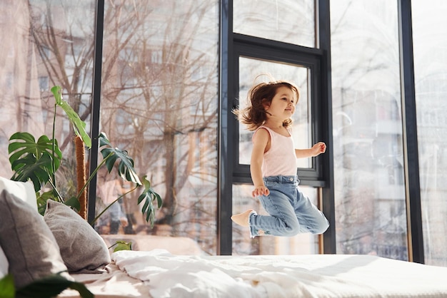 Schattig klein meisje alleen thuis Plezier maken door op het bed te springen