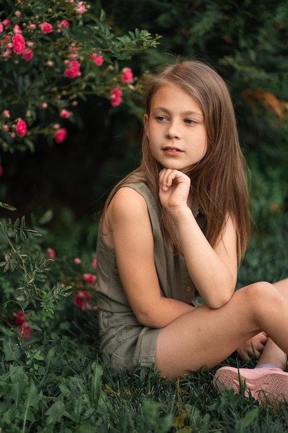 Foto schattig klein meisje buiten zitten in de buurt van een struik rozen