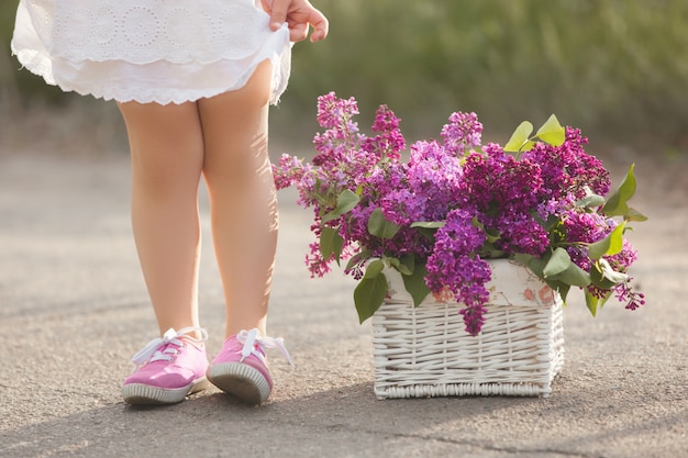 Schattig klein meisje buitenshuis met Lentebloemen. Mooi kind met lila boeket zomertijd. Onherkenbaar kind voeten in sneakers.