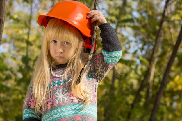 Schattig klein meisje dat als bouwvakker speelt terwijl ze haar veiligheidshelm aanpast terwijl ze nadenkend naar de camera kijkt