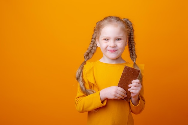 Schattig klein meisje dat chocolade eet op een gele achtergrond