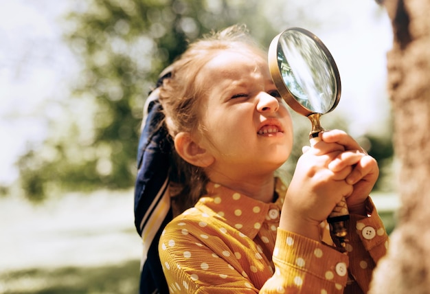 Schattig klein meisje dat de natuur verkent met vergrootglas buiten Kind speelt in het bos met vergrootglas Nieuwsgierig kind kijkt door vergrootglas naar de boom in het park in zonnige dag