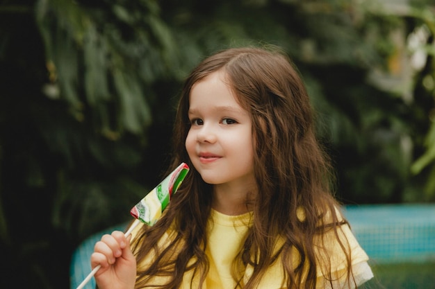 Schattig klein meisje dat een lolly in de vorm van een watermeloen eet kind met lolly's in de botanische tuin