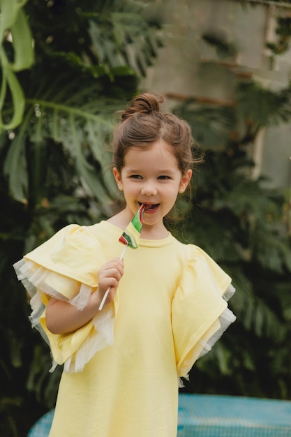 Schattig klein meisje dat een lolly in de vorm van een watermeloen eet Kind met lolly's in de botanische tuin