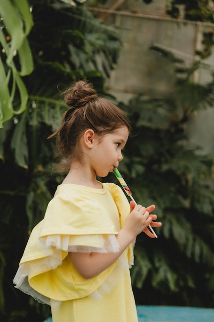 Schattig klein meisje dat een lolly in de vorm van een watermeloen eet Kind met lolly's in de botanische tuin