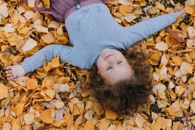 schattig klein meisje dat gele bladeren in het park oplegt in de herfstkaartbanner gezond