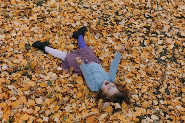 schattig klein meisje dat gele bladeren in het park oplegt in de herfstkaartbanner gezond