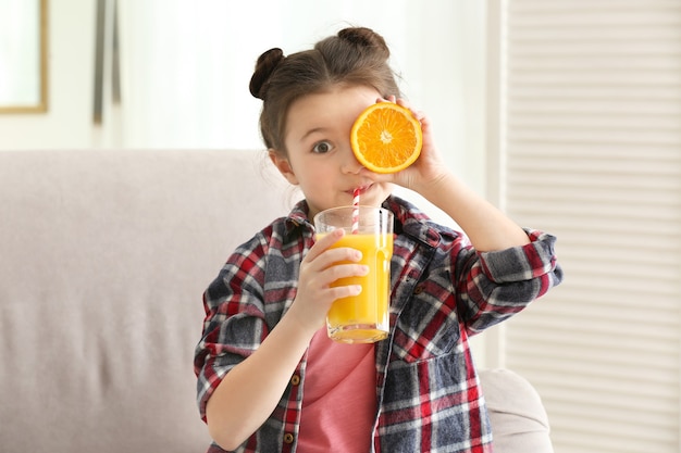 Schattig klein meisje dat sap drinkt terwijl ze thuis op de bank zit