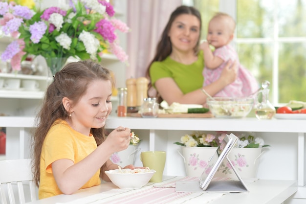 Schattig klein meisje dat verse salade eet aan de keukentafel