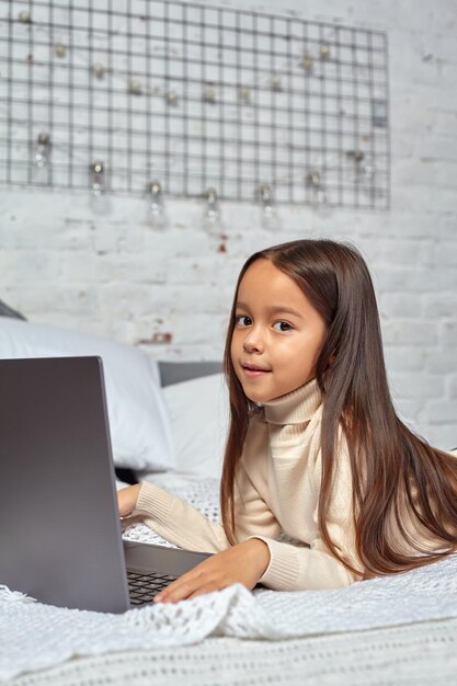 Schattig klein meisje dat zich amusant voelt tijdens het kijken naar tekenfilms op een laptop die op bed zit