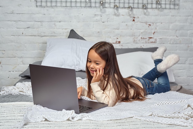 Schattig klein meisje dat zich amusant voelt tijdens het kijken naar tekenfilms op een laptop die op bed zit