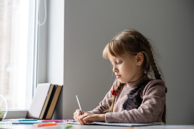 Schattig klein meisje doet haar huiswerk, close-up, op interieur achtergrond