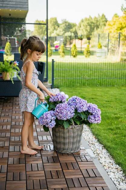 Schattig klein meisje drenken paarse hortensia bloemen uit een gieter in de patio