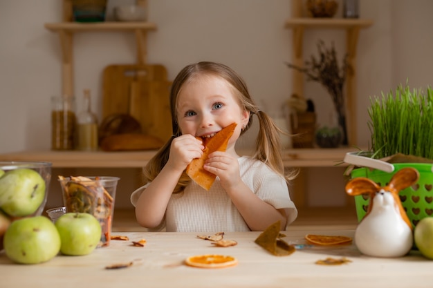 Schattig klein meisje eet natuurlijke pastille thuis in een houten keuken.