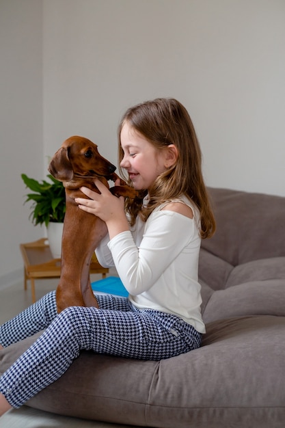 Schattig klein meisje en een dwerg teckel zitten neus aan neus op het bed en kijken elkaar aan