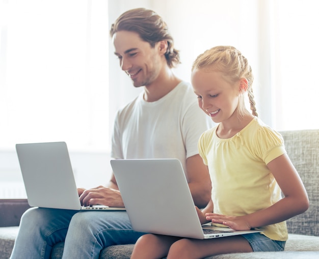 Schattig klein meisje en haar knappe vader gebruiken laptops.