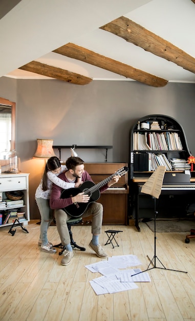 Schattig klein meisje en haar knappe vader spelen gitaar