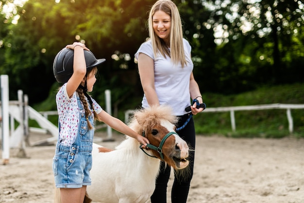 Schattig klein meisje en haar oudere zus genieten met ponypaard buiten op de ranch