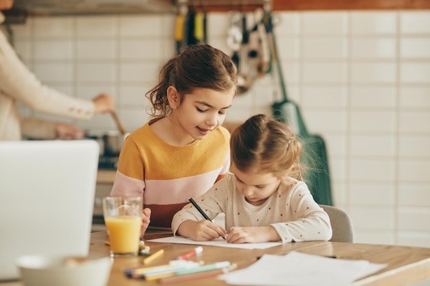 Schattig klein meisje en haar zus tekenen thuis op het papier
