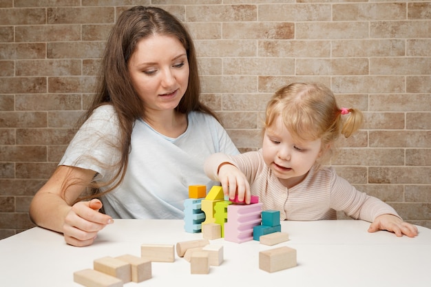 Schattig klein meisje en jonge moeder vrouw spelen met houten speelgoed bouwstenen op tafel