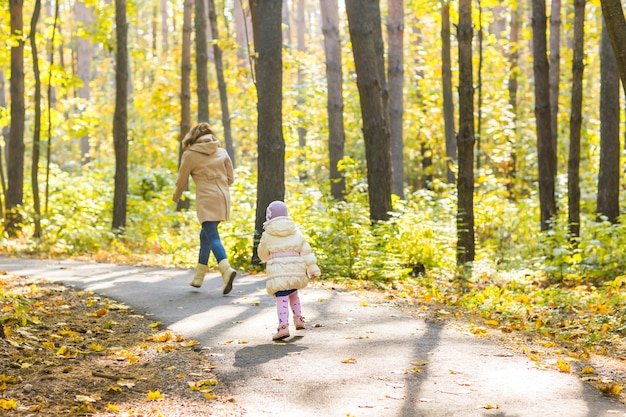 Schattig klein meisje en jonge vrouw in een prachtig herfstbos. Dochter loopt naar moeder. Familieportret, herfstseizoen.
