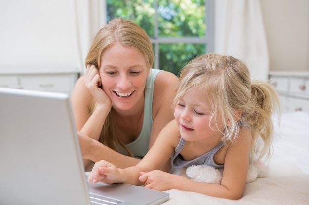 Schattig klein meisje en moeder op bed met behulp van laptop