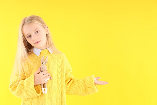 Schattig klein meisje houdt speelgoedkonijn op gele achtergrond