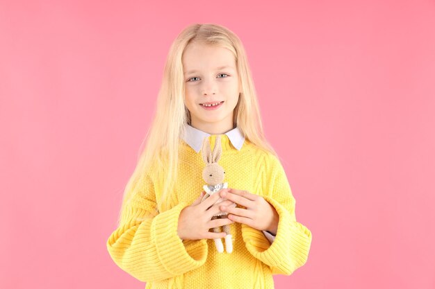 Schattig klein meisje houdt speelgoedkonijn op roze achtergrond