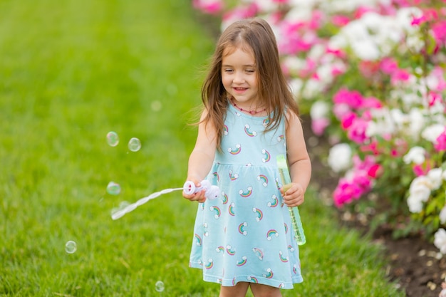 Schattig klein meisje in blauwe jurk met zeepbellen in de zomer van het park