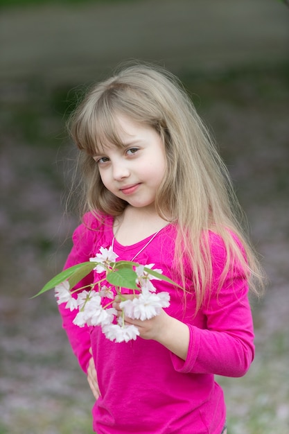 Foto schattig klein meisje in bloeiende kersentuin op mooie lentedag.