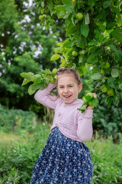 Schattig klein meisje in de takken van een appelboom in zonnige zomerdag
