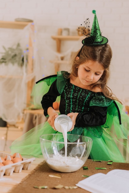 Schattig klein meisje in een groen Halloween-kostuum van een heks of fee bereidt een pompoentaart